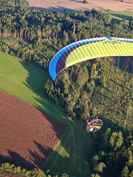 Panoramic aerial view of landscape taken from motorized paraglider, showing open terrain, fields, hills, and wide horizon under clear or partly cloudy sky.