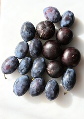 Close-up top view of assorted blue plums showcasing various types and natural shades of blue and purple. A vibrant mix of textures and colors on a clean white background.