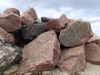 Pile of large colorful rocks under cloudy sky at beach  