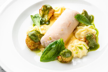 Gourmet plated dish with rolled white meat, creamy puree, roasted vegetables, green herb sauce, and fresh leafy garnish. Elegant fine dining presentation