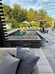 Beautiful, luxury, modern backyard lounge area. Umbrella, sofa, lounge chairs table poolside. Hotel resort feel. Seating and tanning sundeck by gray stone pavers. Fire pit and waterfall. High end. Beautiful, luxury, modern backyard lounge area. Umbrella, sofa, lounge chairs table poolside. Hotel resort feel. Seating and tanning sundeck by gray stone pavers. Fire pit and waterfall. High end.
