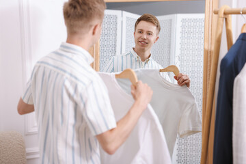 Fototapeta premium Getting ready. Young man trying on clothes near mirror at home