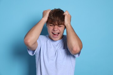 Fototapeta premium Teenage boy suffering from panic attack on light blue background