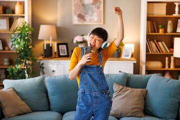 Woman having fun listening to the music, singing and dancing while relaxing at home