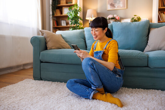 Woman using smart phone while relaxing at home - Powered by Adobe