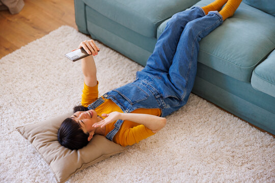 Woman having video call using smart phone while relaxing at home
