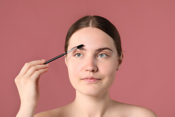 Fototapeta premium Young woman brushing her eyebrow with spoolie on pink background