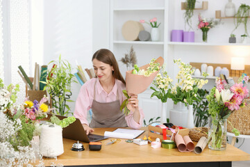 Professional florist working with laptop at wooden table in shop