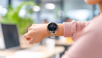 Close-up of a woman's hand wearing a smartwatch, with a blurred office background.