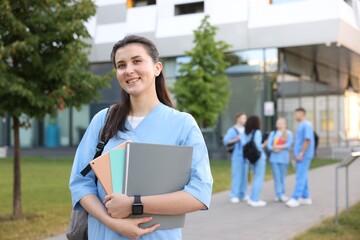 Fototapeta premium Medical student in uniform with backpack and notebooks outdoors, selective focus
