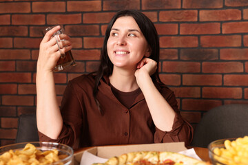 Young woman with glass of beer at table with food in bar