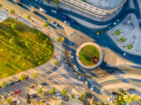 Top-down aerial view of a busy roundabout with cars, palm trees, and urban architecture in Durrës, Albania, during golden hour. - Powered by Adobe