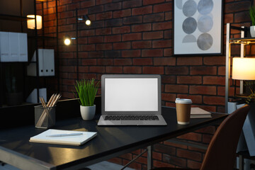 Laptop, takeaway paper cup, houseplants and stationery on black table near brick wall