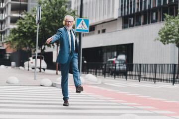 Obraz premium Confident businessman walking outdoors in a city street, wearing formal suit and headphones while smiling and enjoying the day