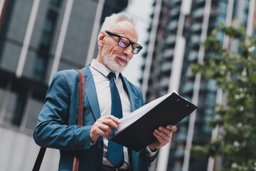 Successful senior business professional reviewing documents in a modern urban environment wearing a stylish formal suit