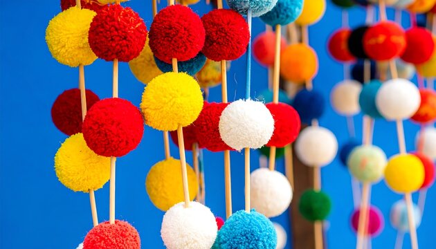 Colorful pom-poms strung on wooden skewers against a vibrant blue background.