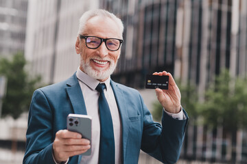 Confident senior businessman holding smartphone and card outdoors showcasing successful career and modern technology