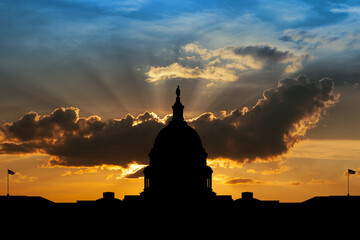 The United States Capitol building silhouette on background of sky at sunset with flying birds in Washington DC, USA