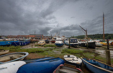 Small boats under a stormy sky. View of the quay at low tide on the River Deben in the historic town of Woodbridge in Suffolk, UK.