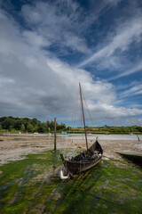 Old wooden boat with mast sitting on mud. View of the quay at low tide on the River Deben in the historic town of Woodbridge in Suffolk, UK.