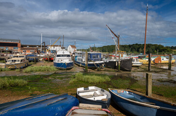 Small boats on a sunny day. View of the quay at low tide on the River Deben in the historic town of Woodbridge in Suffolk, UK.