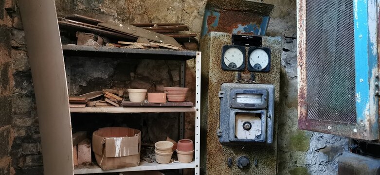Derelict factory workshop. Shelves, rusted panel, vintage gauges, abandoned pots. Pareidolia example, seeing faces in inanimate objects. Rusty old equipment, meter dials. Smiling android robot face.