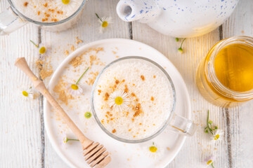 Calming natural chamomile flowers tea latte, organic late night cozy warm beverage with milk and floral chamomile tea, with honey and ginger spices