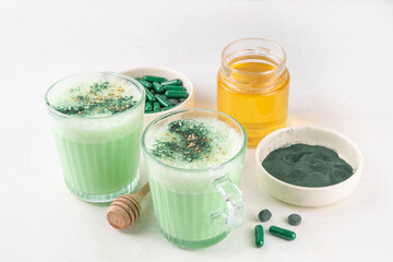 Healthy spirulina latte drink. Caffeine-free green spirulina infused, calming beverage, with spirulina powder, pills and capsules on white table background