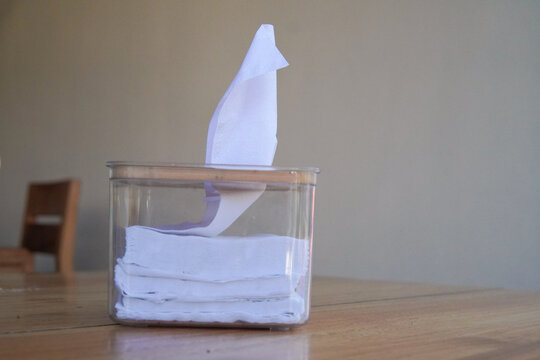 Small box with white tissues inside sits on a wooden table in a cafe or restaurant.