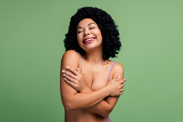 Attractive young woman embracing herself, radiating joy and self-love in a green background, celebrating natural beauty and diversity