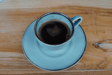 Obraz premium A cup of black coffee or Americano in a blue cup, isolated by wood background.
