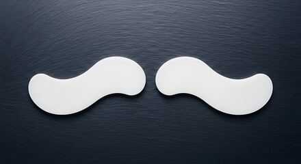 A pair of white hydrogel under-eye patches for puffy eyes and dark circles, displayed on a dark slate background.