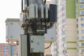 Electrical boxes and communication equipment mounted on a pole with a residential high-rise building in the background.
