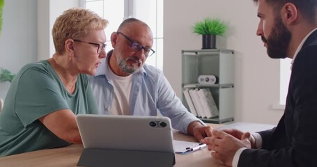 Senior couple consults financial advisor using digital tablet and documents in bright office. Professional meeting moment. They review investment options and future plans together. - Powered by Adobe