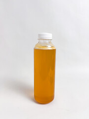 Transparent plastic bottle containing golden-colored honey with a white lid, standing on a white background
