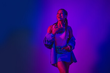 Fashionable young woman enjoying the neon glow with a trendy denim outfit, exuding confidence and charm under vibrant purple lighting.