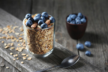 Granola and fresh blueberries in glass bowl over old wood background.
