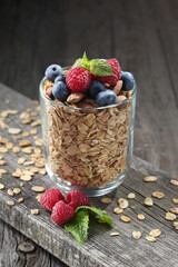 Granola with fresh blueberries and raspberries in glass bowl over old wood background.