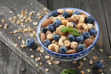 Granola with nuts and fresh blueberries in glass bowl over old wood background.