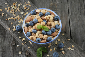 Granola with nuts and fresh blueberries in glass bowl over old wood background.