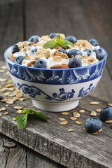Granola with yogurt and fresh blueberries in glass bowl over old wood background