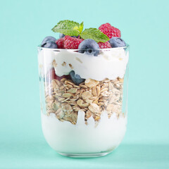 Granola with yogurt, fresh blueberries and raspberries on mint background