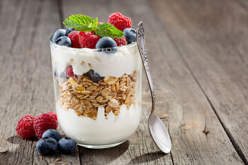 Granola with yogurt, fresh blueberries and raspberries in glass over old wood background.