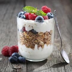 Granola with yogurt, fresh blueberries and raspberries in glass over old wood background.