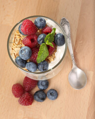 Granola with yogurt, fresh blueberries and raspberries in glass over wood background.