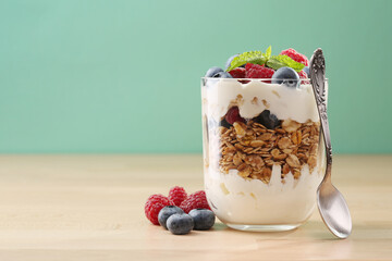 Granola with yogurt, fresh blueberries and raspberries in glass on wood background