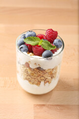 Granola with yogurt, fresh blueberries and raspberries in glass over wood background.