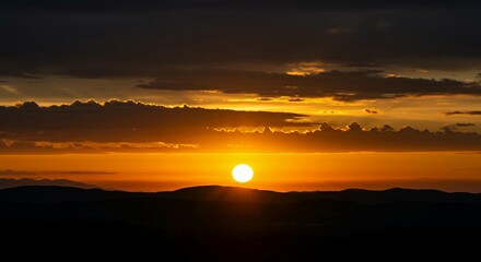 Vibrant orange and gold sunset sky with dramatic cloud layers over mountain ridges silhouette creating stunning natural landscape scene