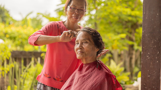 Community hairstylist offers personal haircut to elderly woman in a lush outdoor setting during a sunny day