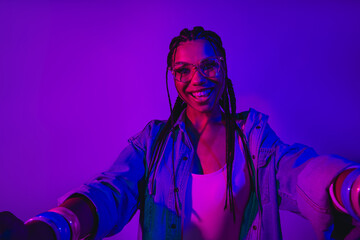 Woman enjoying vibrant neon lighting wearing trendy denim jacket and stylish glasses with playful expression